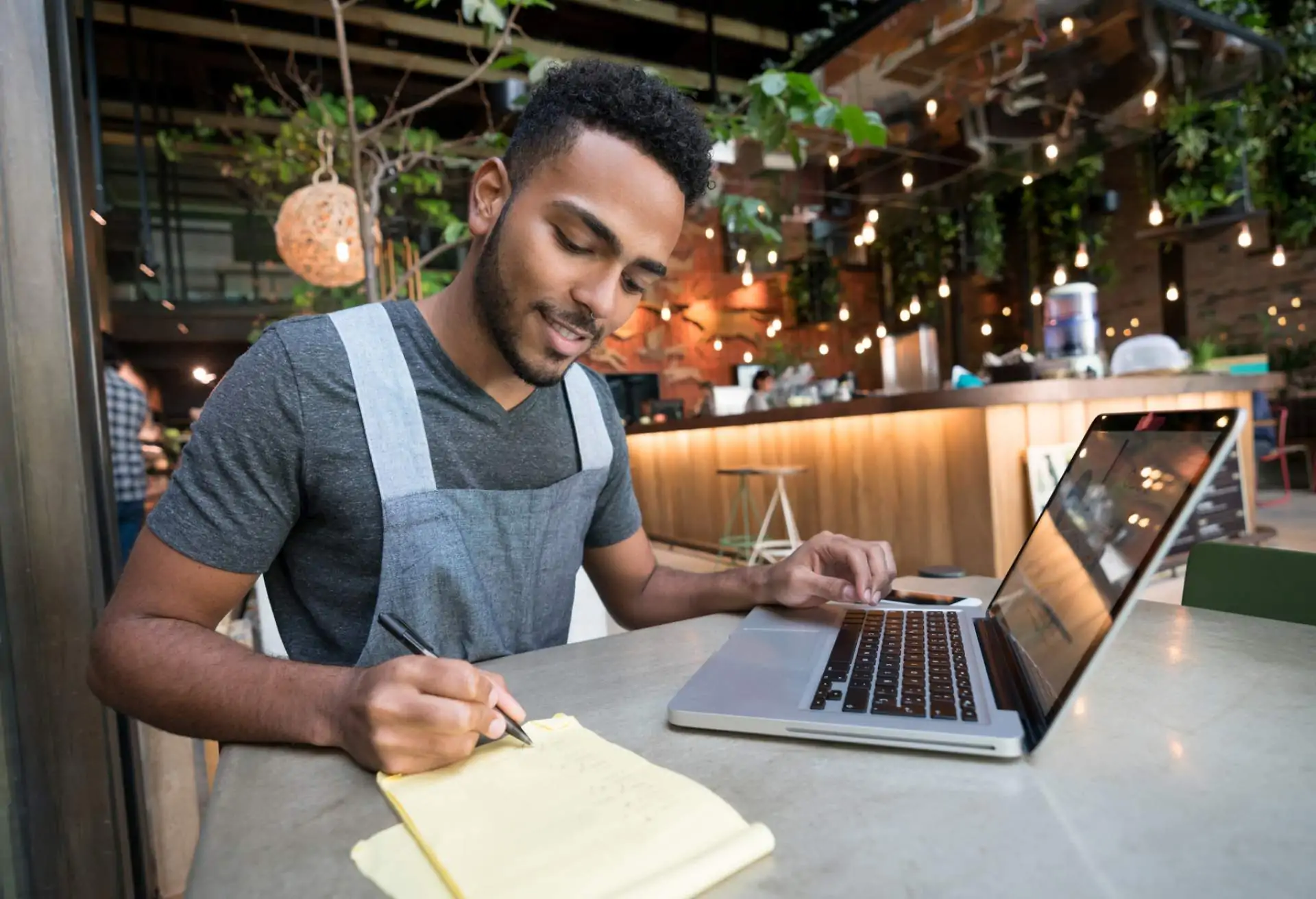 A restaurant worker is compiling some paperwork while working on their laptop